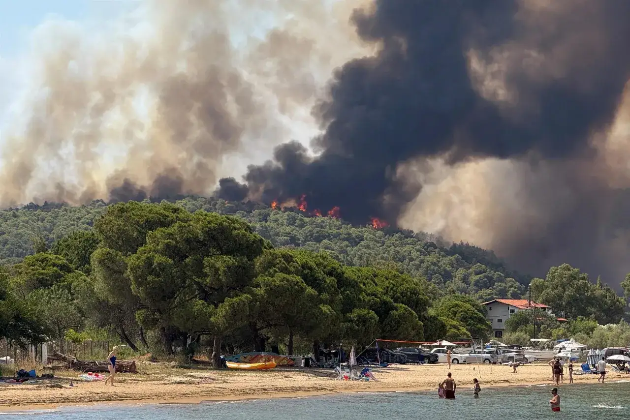Dym z pożaru lasu nad zatoką. Ludzie na plaży, zastanawiają się, czy na Krecie jest bezpiecznie.