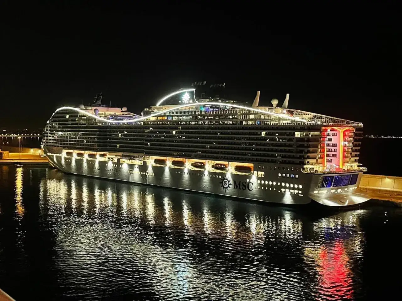 MSC World Europa, un gigante del mare, illumina la notte in un porto europeo.