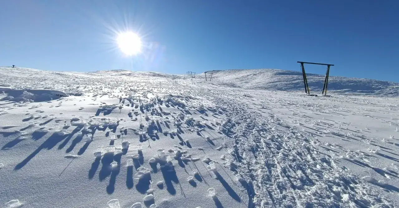 Sole splendente sulla **monte piselli stazione sciistica**. Tracce sulla neve e pali di un impianto di risalita.