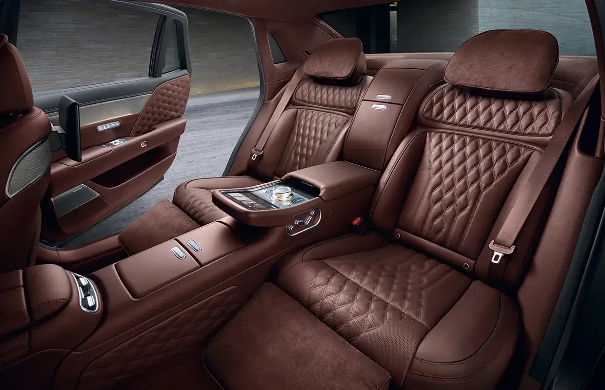Asientos de cuero marr&oacute;n con dise&ntilde;o acolchado, consola central con pantalla y controles, y detalles de lujo en el interior de un Mercedes.