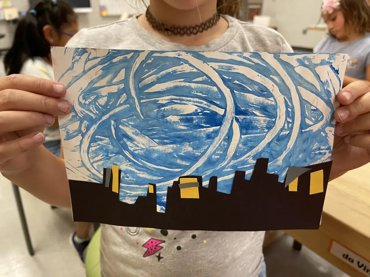 Niños crean manualidades inspiradas en Van Gogh: un cielo azul arremolinado sobre un horizonte urbano.