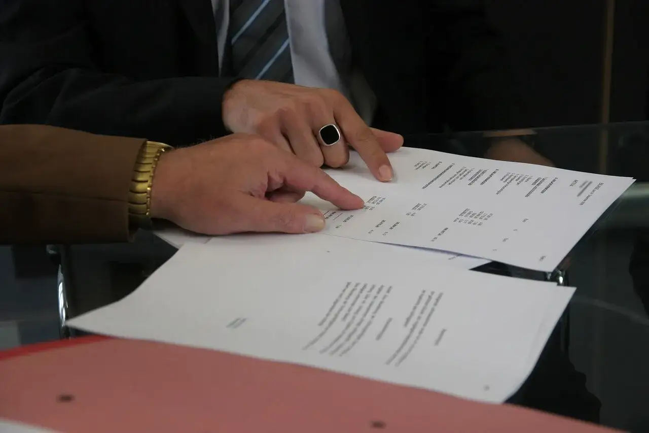Dw&oacute;ch mężczyzn analizuje dokumenty. Jeden z nich, w garniturze i z sygnetem, wskazuje palcem na tabelę. Pytanie: Millennium Bank zajęcie egzekucyjne jak sprawdzić?