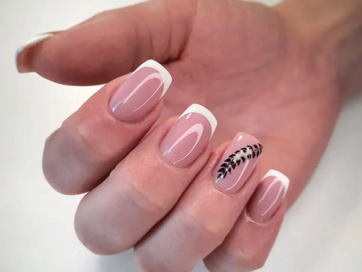 Dłoń z paznokciami żelowymi w naturalnych kolorach. Klasyczny french manicure z subtelnym zdobieniem w postaci czarnej gałązki na jednym paznokciu.