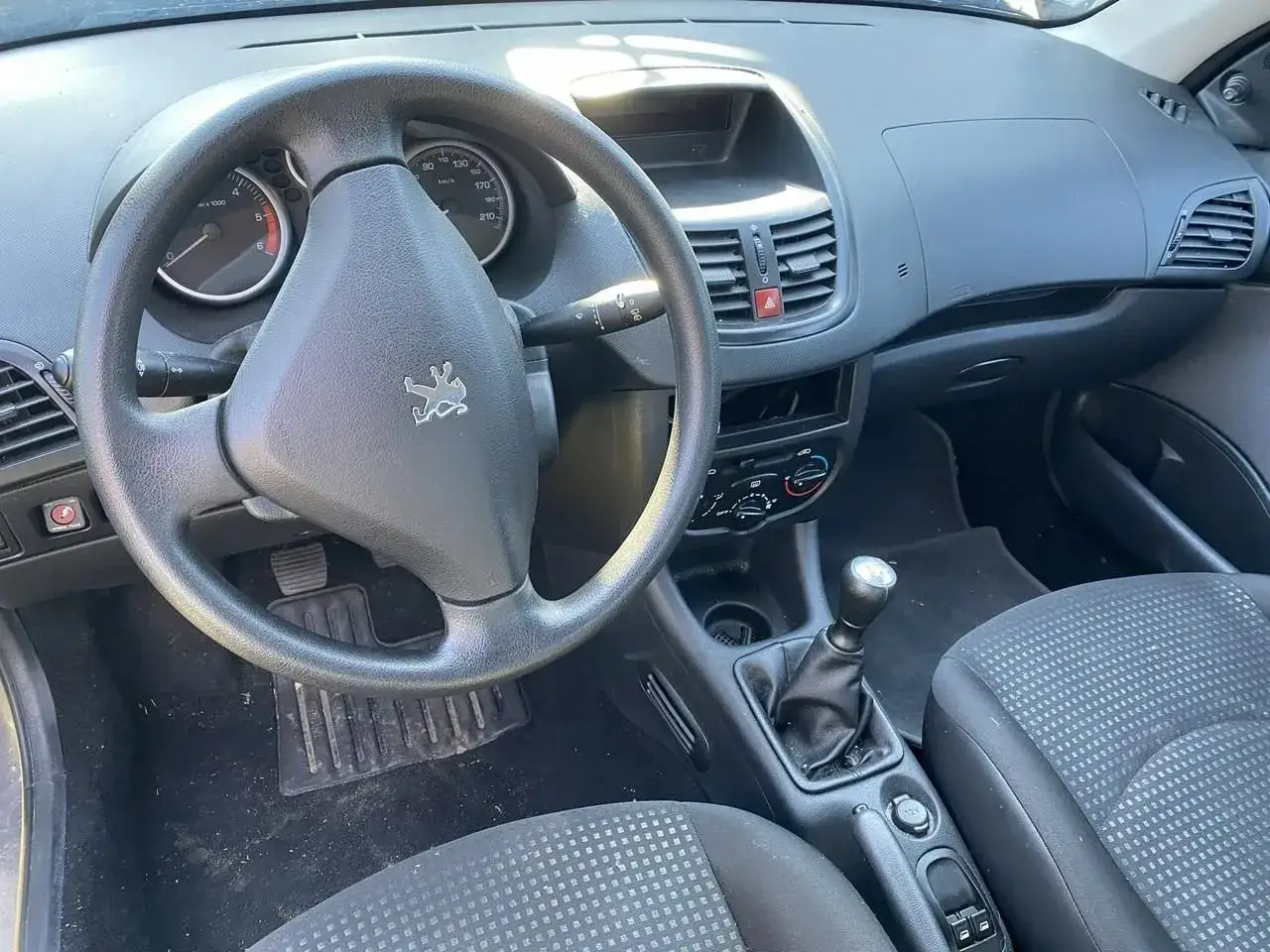 Wnętrze Peugeot 206 Plus: kierownica z logo, deska rozdzielcza, dźwignia zmiany biegów i siedzenie pasażera.