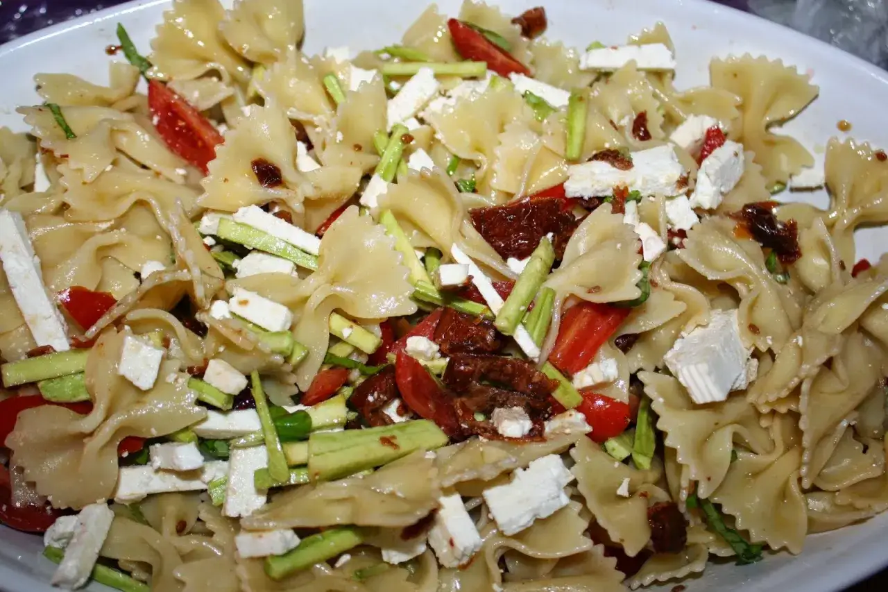Un'appetitosa insalata di pasta con farfalle, pomodorini, zucchine, feta e pomodori secchi.