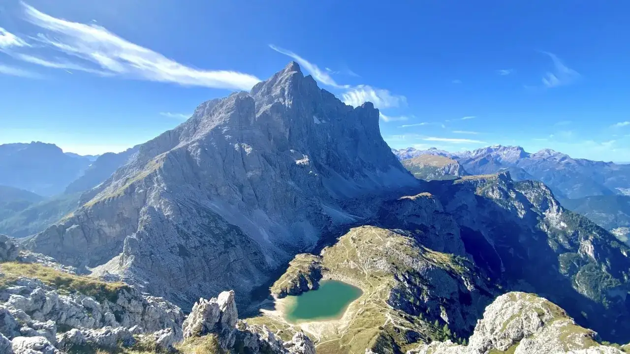 Un incantevole **lago Coldai** incastonato tra le maestose vette delle Dolomiti, sotto un cielo azzurro solcato da nuvole leggere.