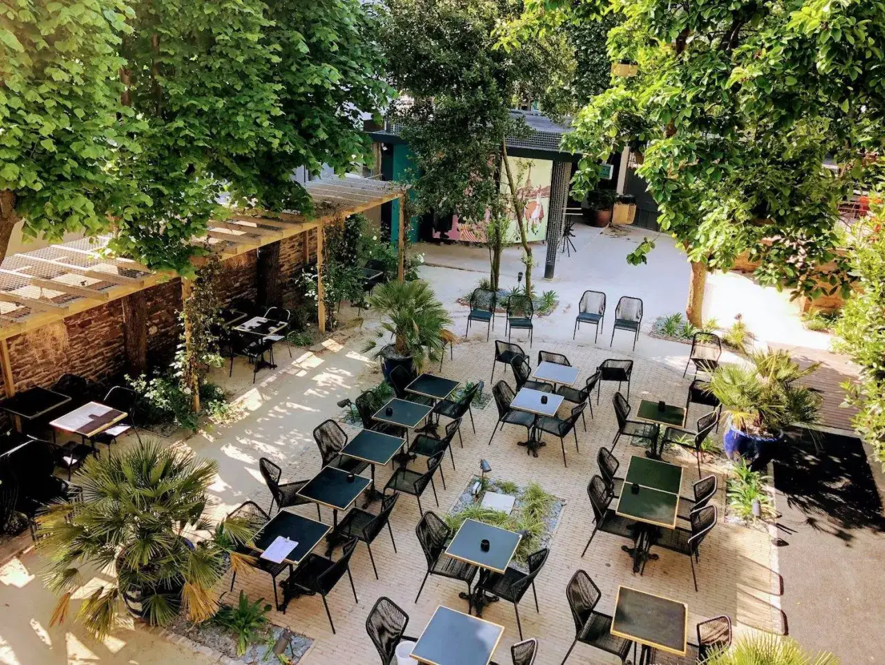 Terrasse ensoleillée d'un resto ouvert le dimanche à Rennes. Tables dressées sous les arbres, ambiance estivale.