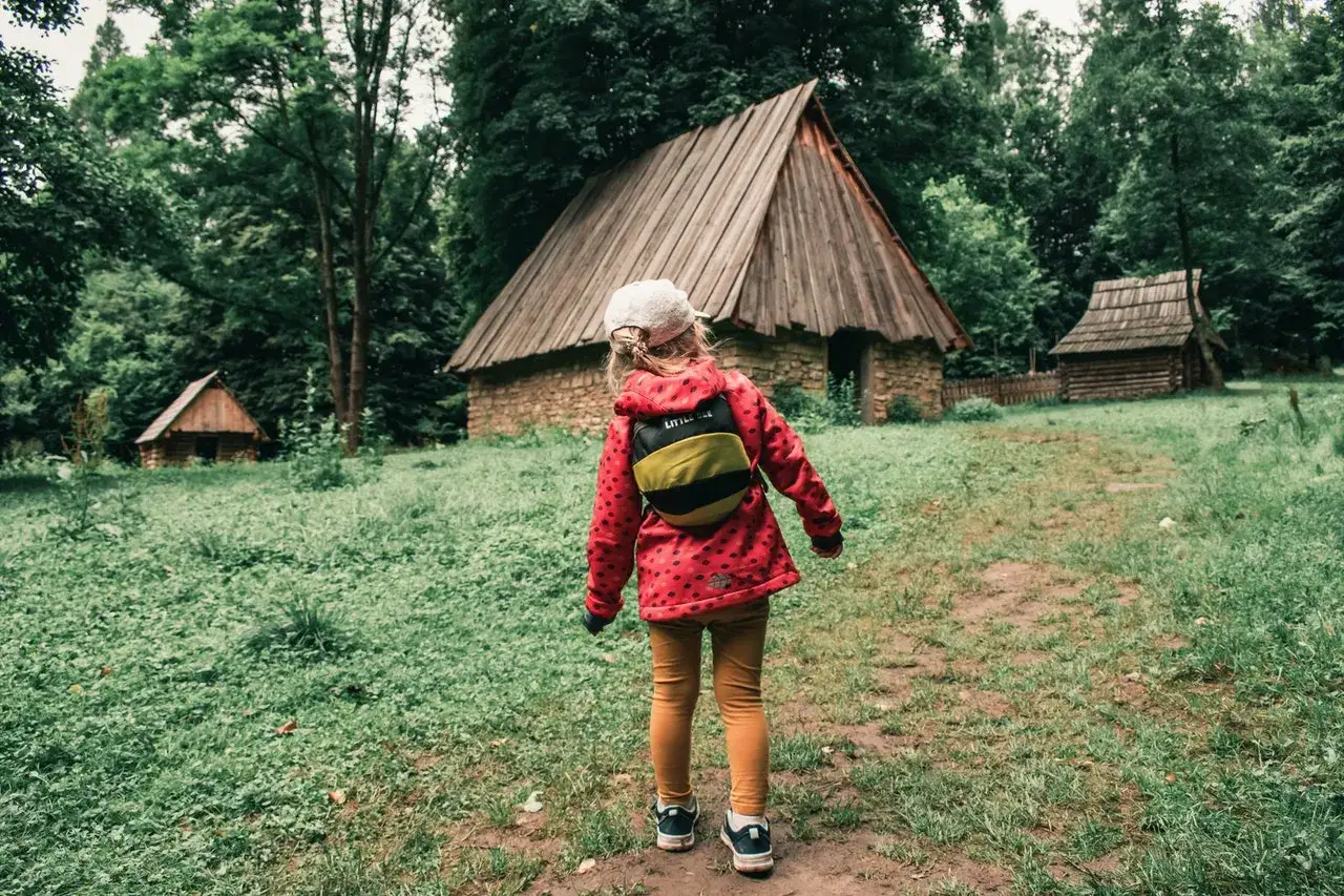 Dziewczynka w czerwonej kurtce odkrywa sokołowskie atrakcje – drewniane chaty w otoczeniu zieleni.