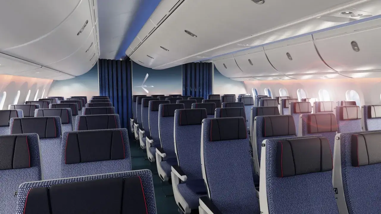 Wnętrze samolotu Dreamliner, rzędy niebieskich foteli z czarnymi zagłówkami i czerwonymi akcentami. Widok na niebo za oknami.