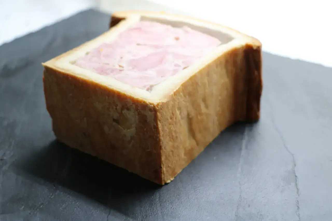 Un pâté en croûte d'origine, avec sa garniture rose et sa croûte dorée, repose sur une surface sombre.