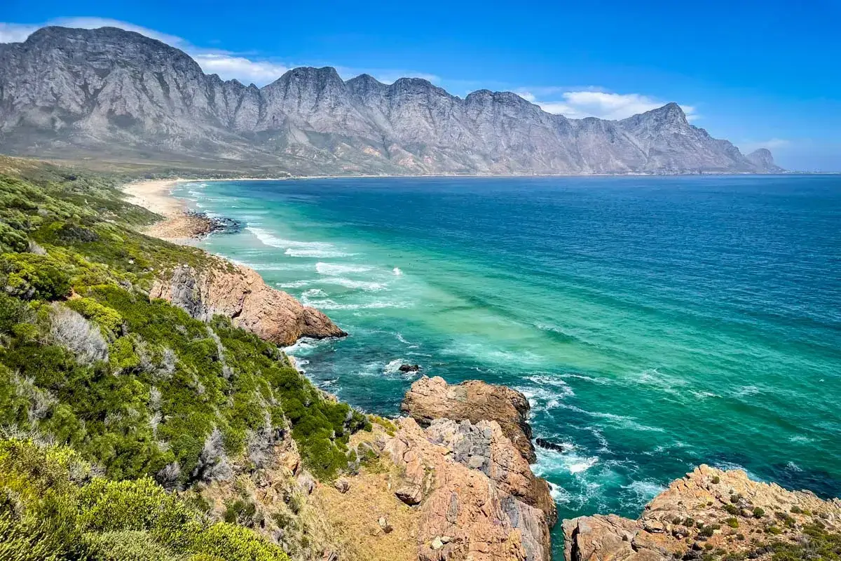 Atemberaubende Küstenlandschaft der Garden Route Kapstadt. Türkisfarbenes Meer trifft auf felsige Klippen und grüne Vegetation.