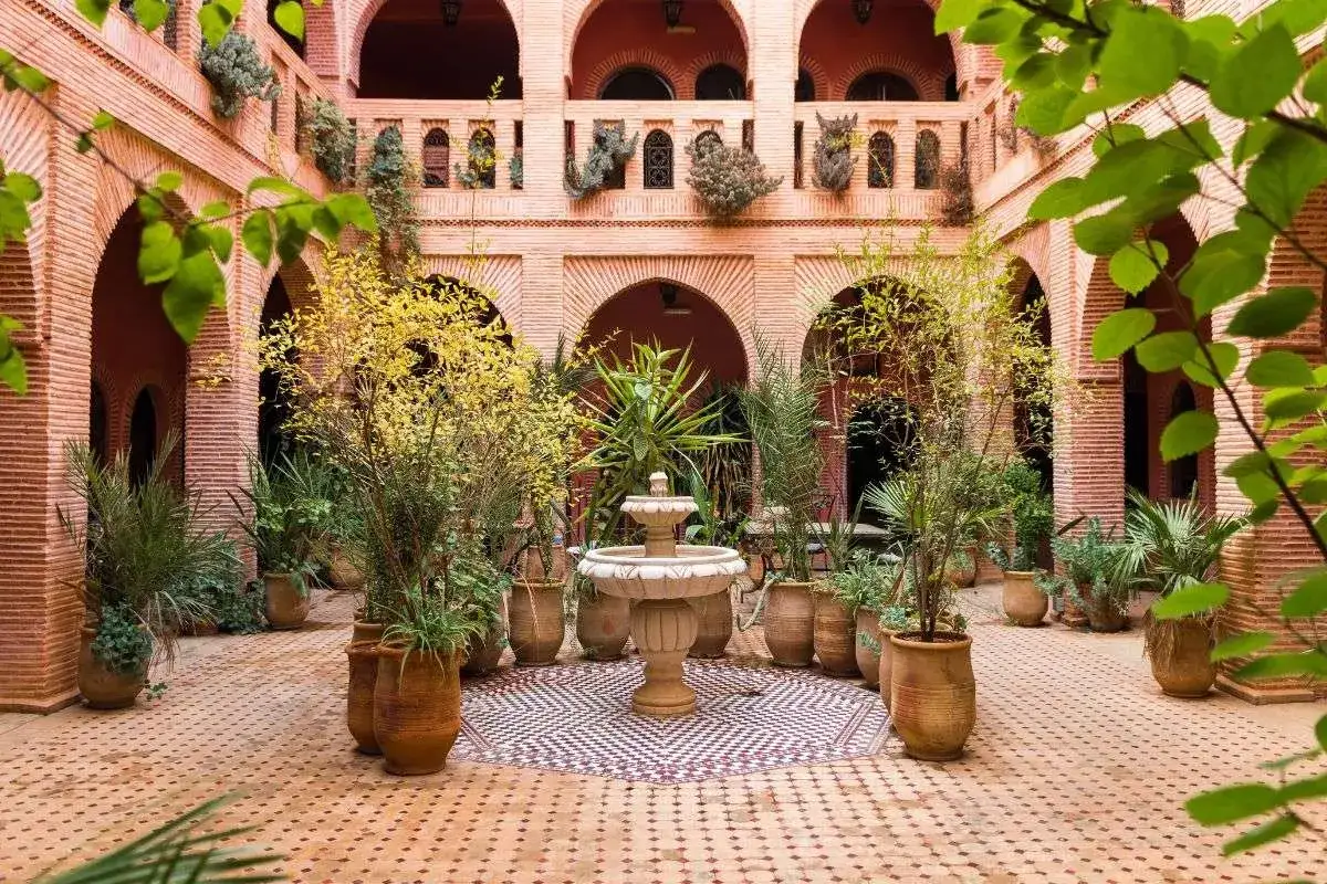 Ein Riad in Marokko: Ein Innenhof mit Brunnen, umgeben von Ziegelb&ouml;gen und &uuml;ppiger Vegetation, ein Ort der Ruhe.