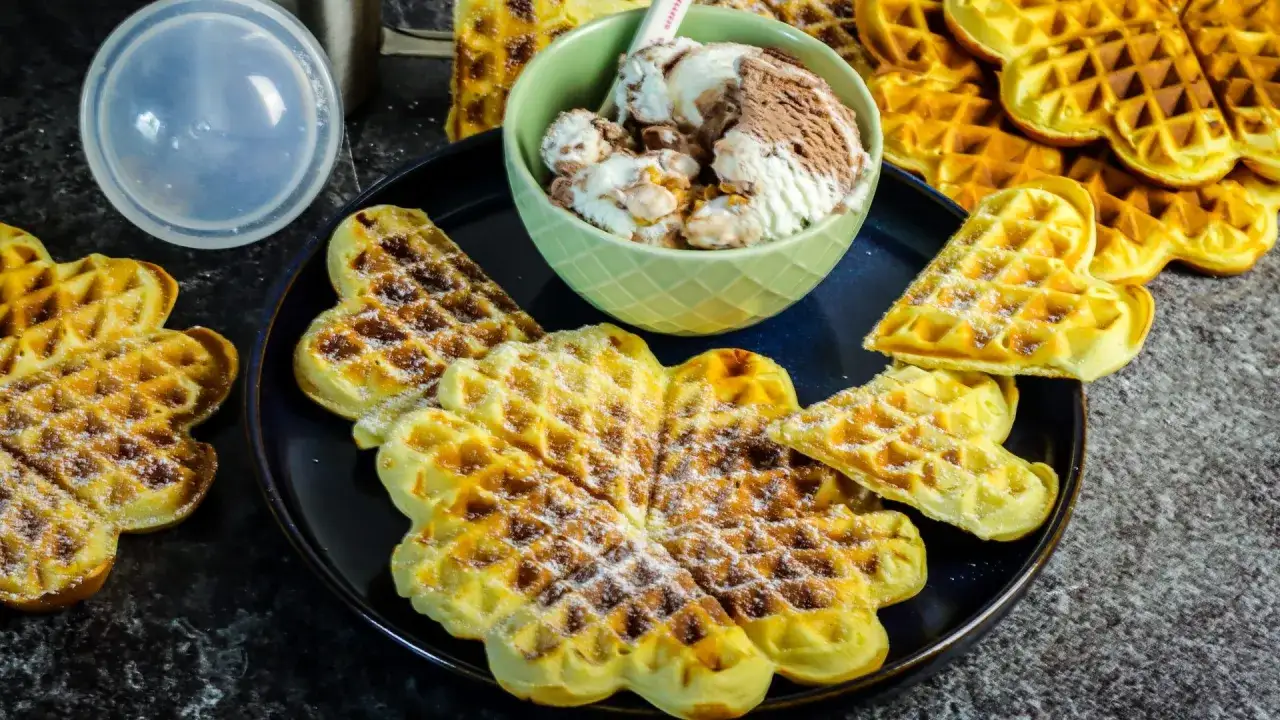 Herzförmige Waffeln ohne Ei, bestäubt mit Puderzucker, serviert mit einer Schüssel Eiscreme. Ein Genuss für alle!
