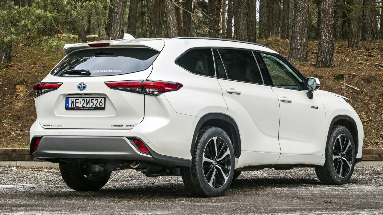Biały Toyota Highlander Hybrid AWD na leśnej drodze. Zwróć uwagę na jego imponujące wymiary i stylowe detale.
