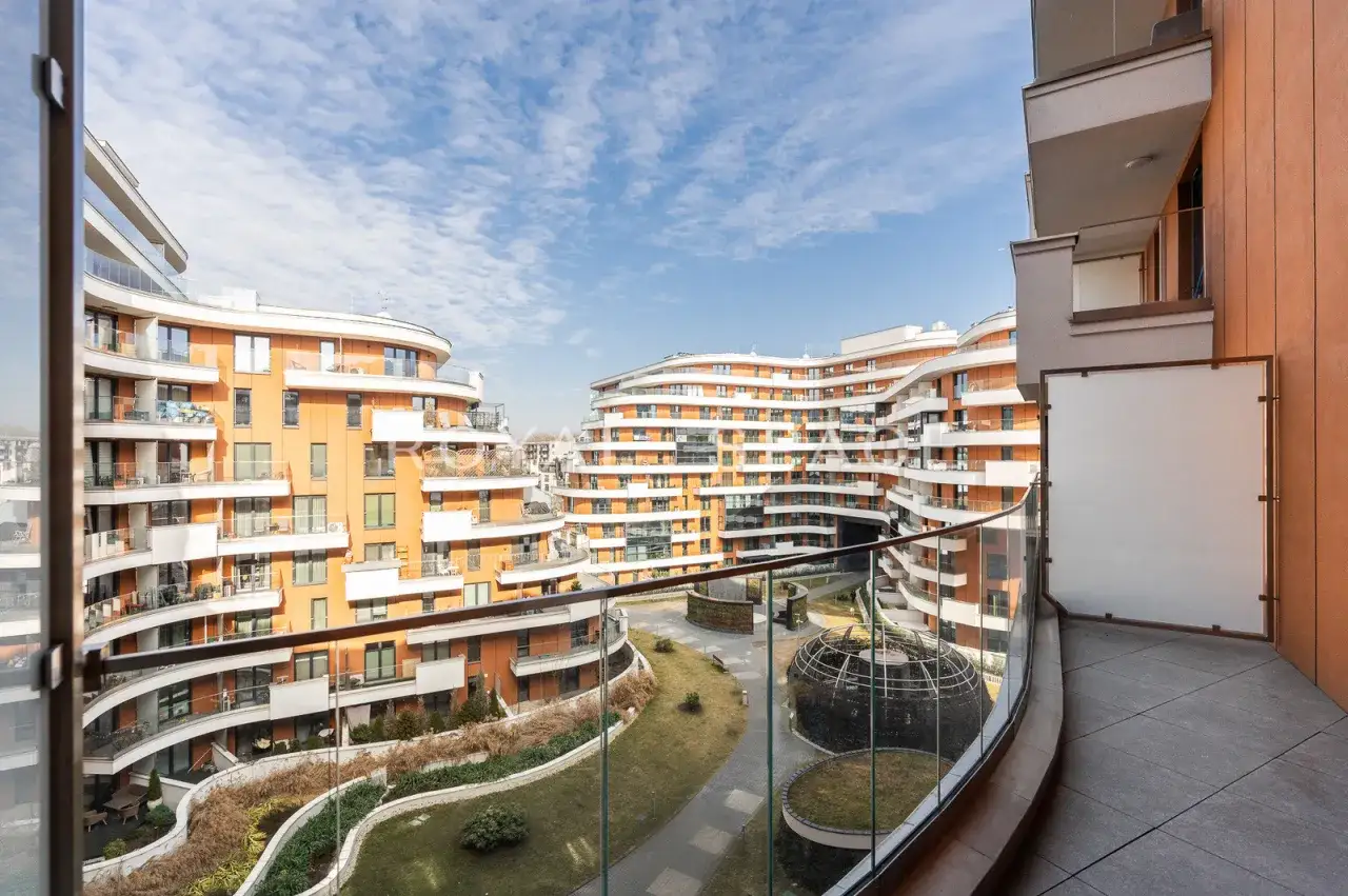 Nowoczesny apartamentowiec z pomarańczowymi fasadami i balkonami tworzy łuk wokół zielonego dziedzińca.