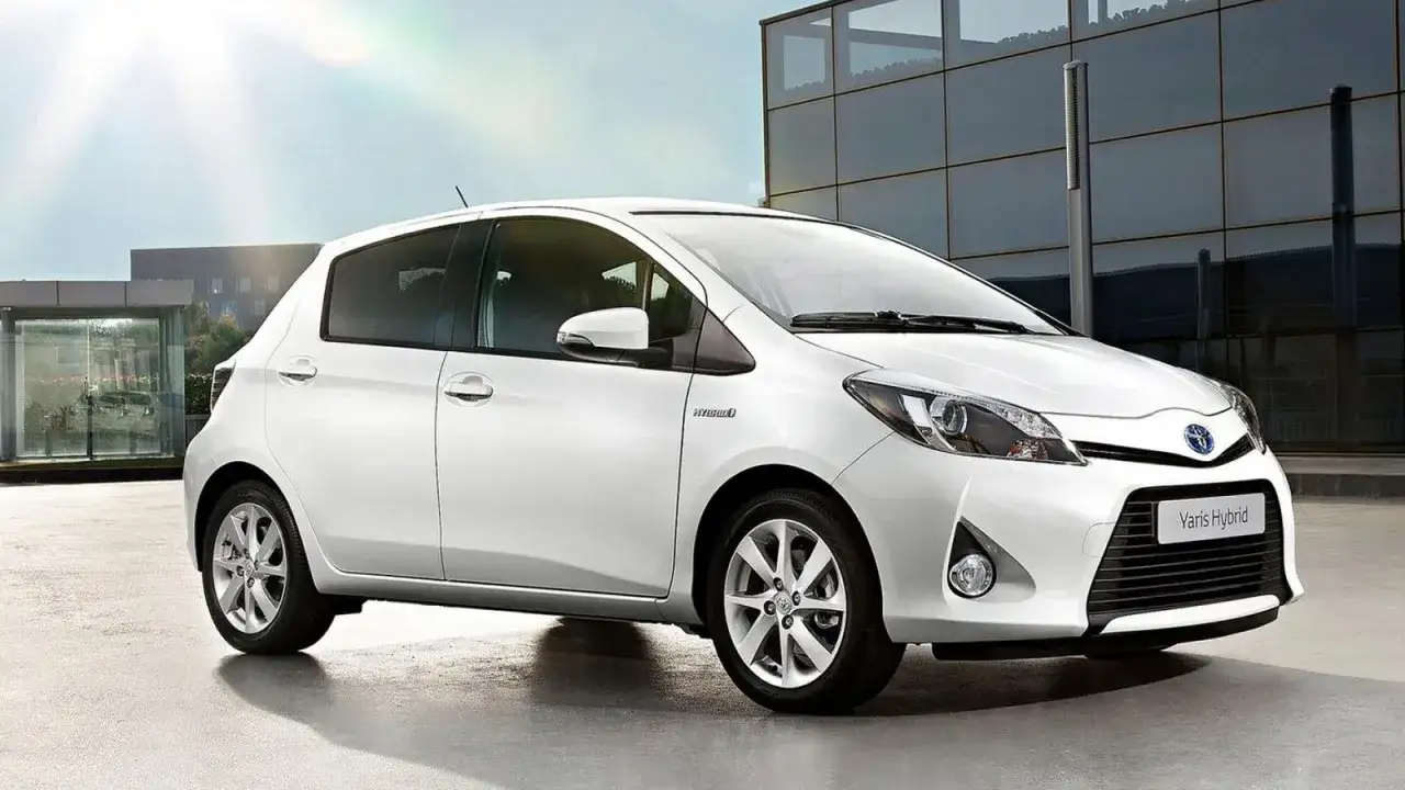 Vit Toyota Yaris Hybrid står parkerad framför en modern byggnad. Kanske är det en ny bil, eller så har den ett oväntat toyota yaris hybrid problem.