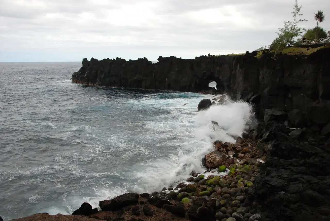 Costa rocosa de la isla Reuni&oacute;n, con olas rompiendo contra las rocas. El mar agitado y los acantilados imponentes sugieren los peligros de esta isla.