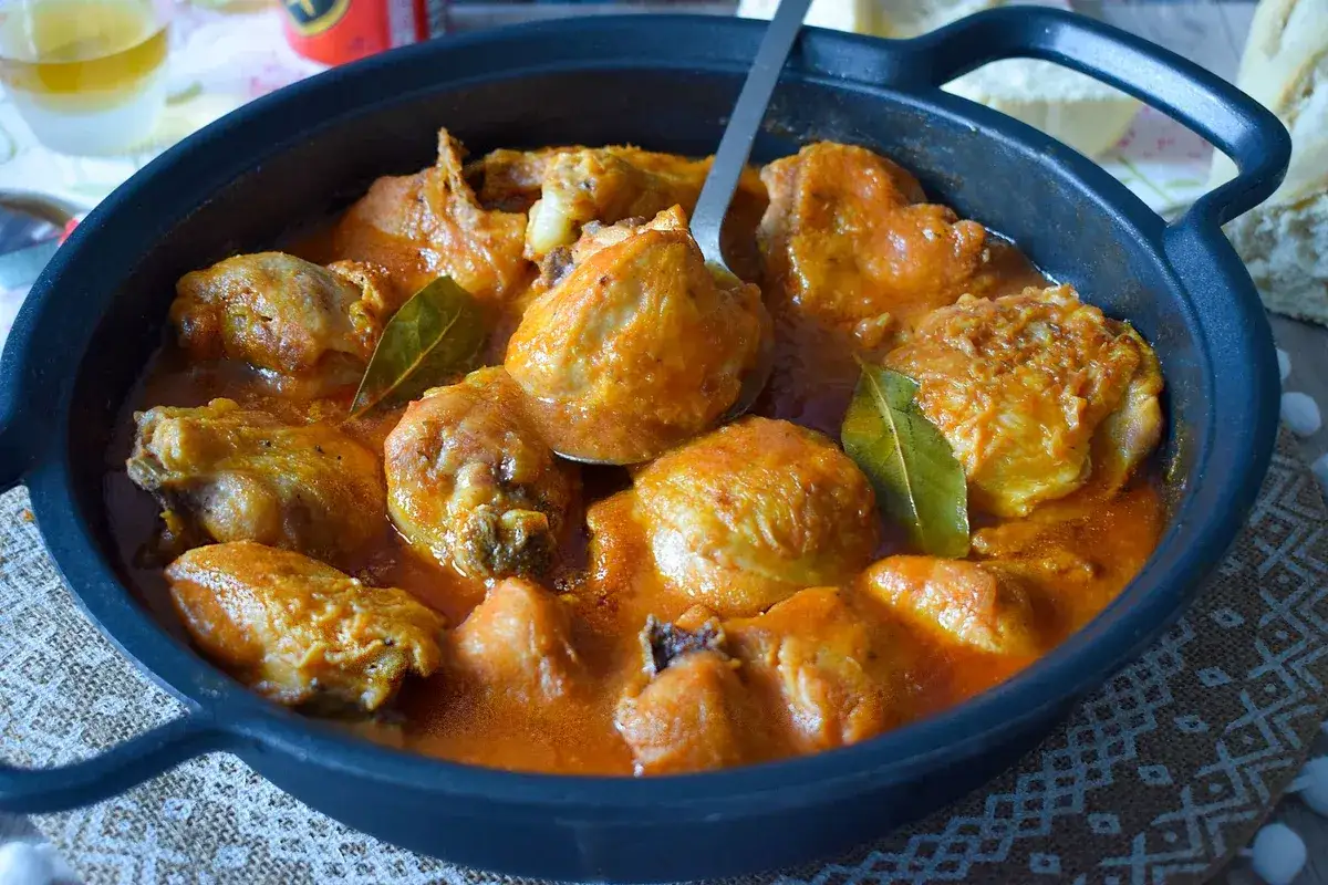 Sabroso pollo a la cerveza en cazuela negra, con salsa naranja y hojas de laurel.