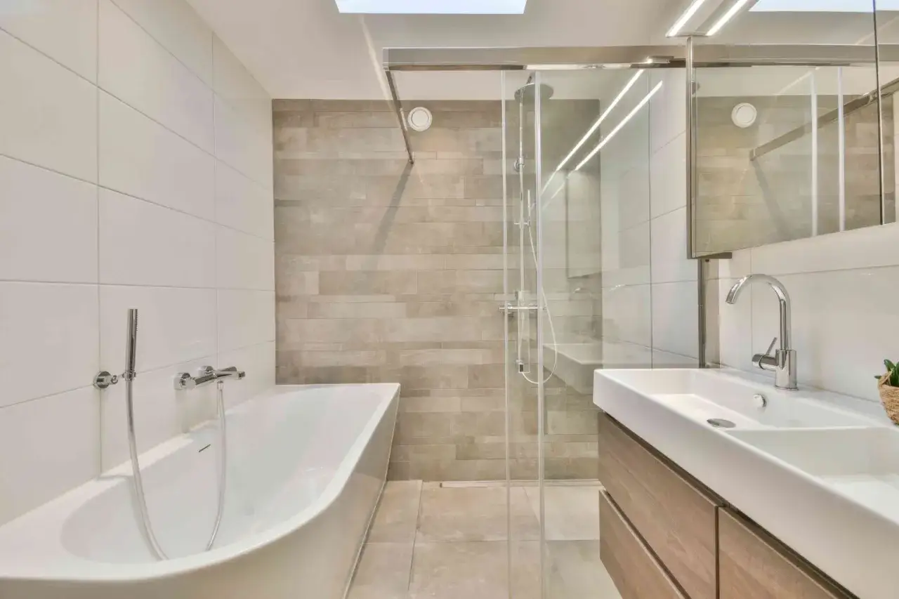 Bagno moderno con vasca freestanding, doccia con box in vetro e lavabo sospeso. Idee su come rivestire un bagno con piastrelle bianche e beige.