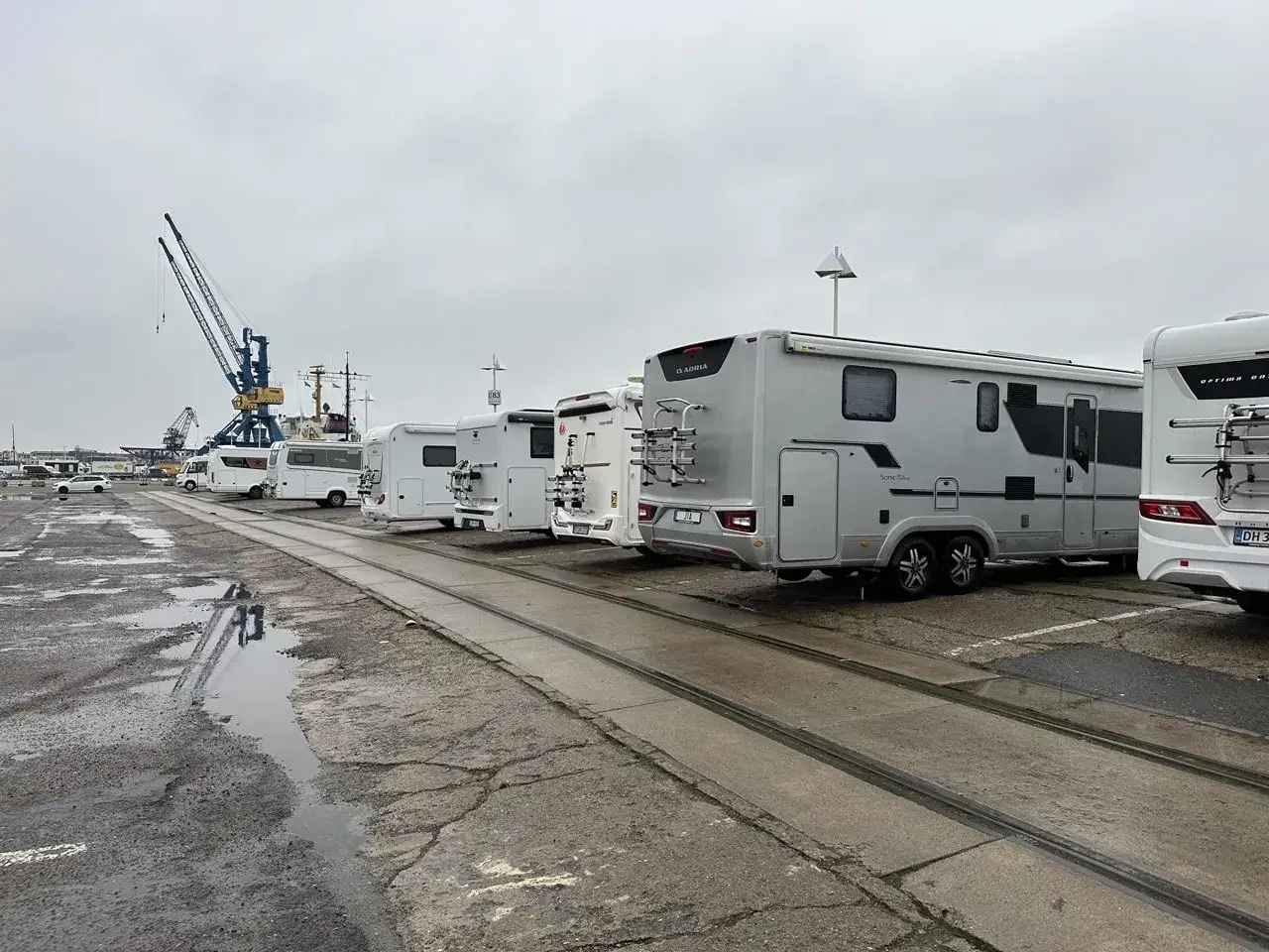 Rad med husbilar vid en hamn, kanske en paus p&aring; resan till en autohof i Tyskland. Kranar syns i bakgrunden.