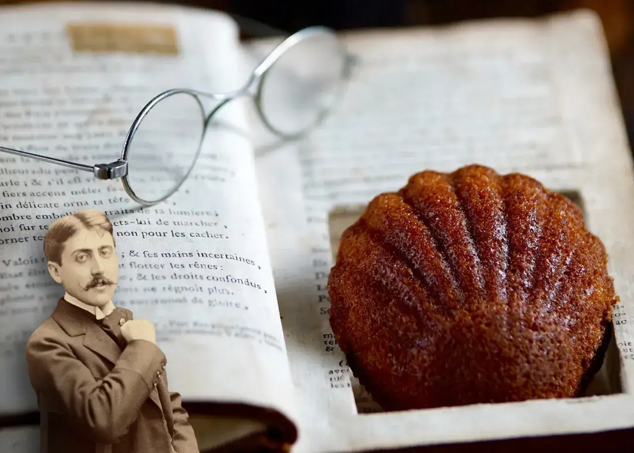 Un retrato de Marcel Proust junto a una madeleine de Proust, unas gafas y un libro abierto.