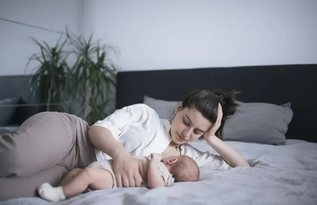 mama karmiąca dziecko piersią na leżąco w łóżku z poduszkami