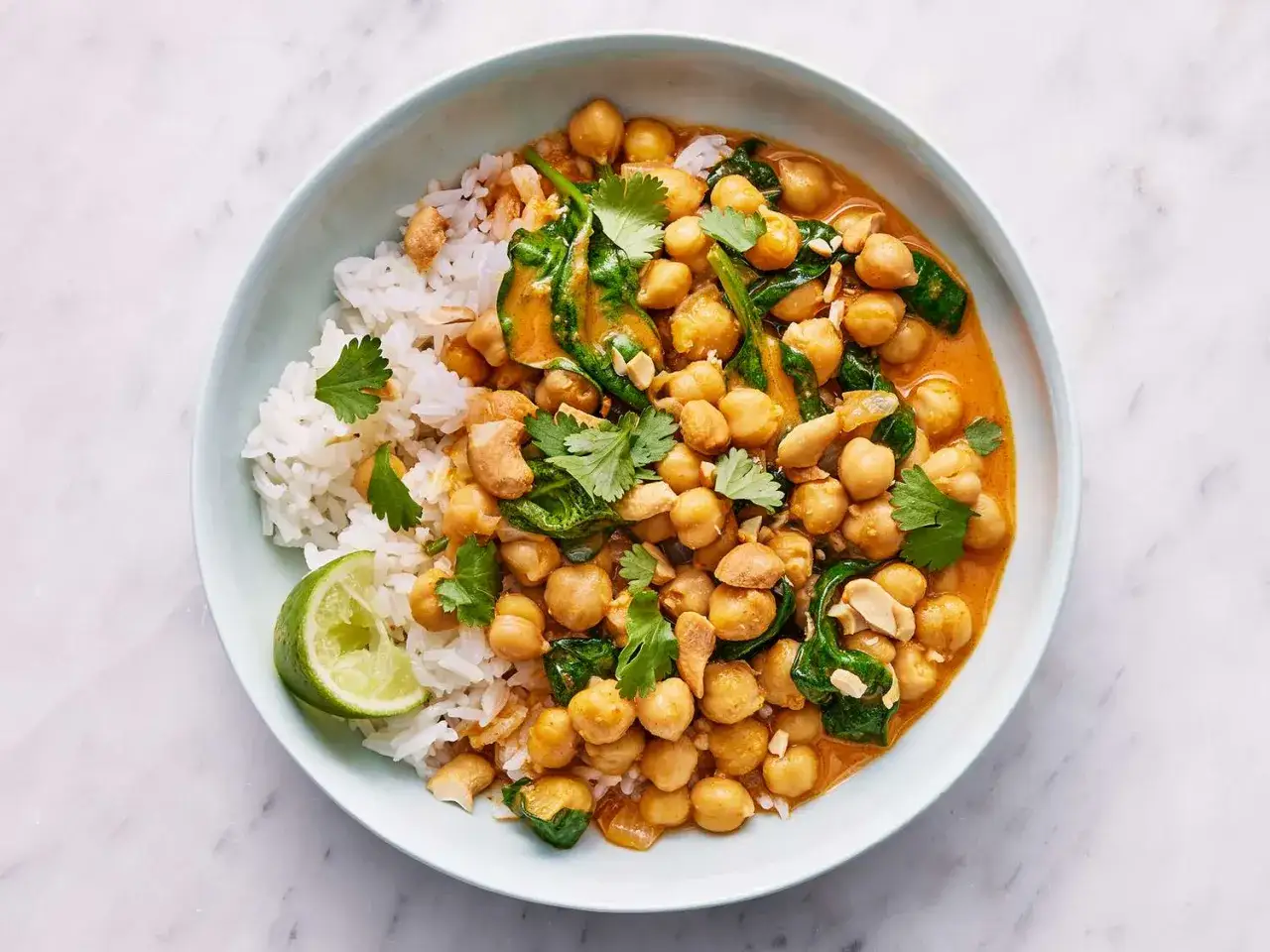 Schüssel mit Reis und cremigem, veganem Curry mit Kichererbsen, Spinat und Cashewkernen, garniert mit Koriander und Limette.