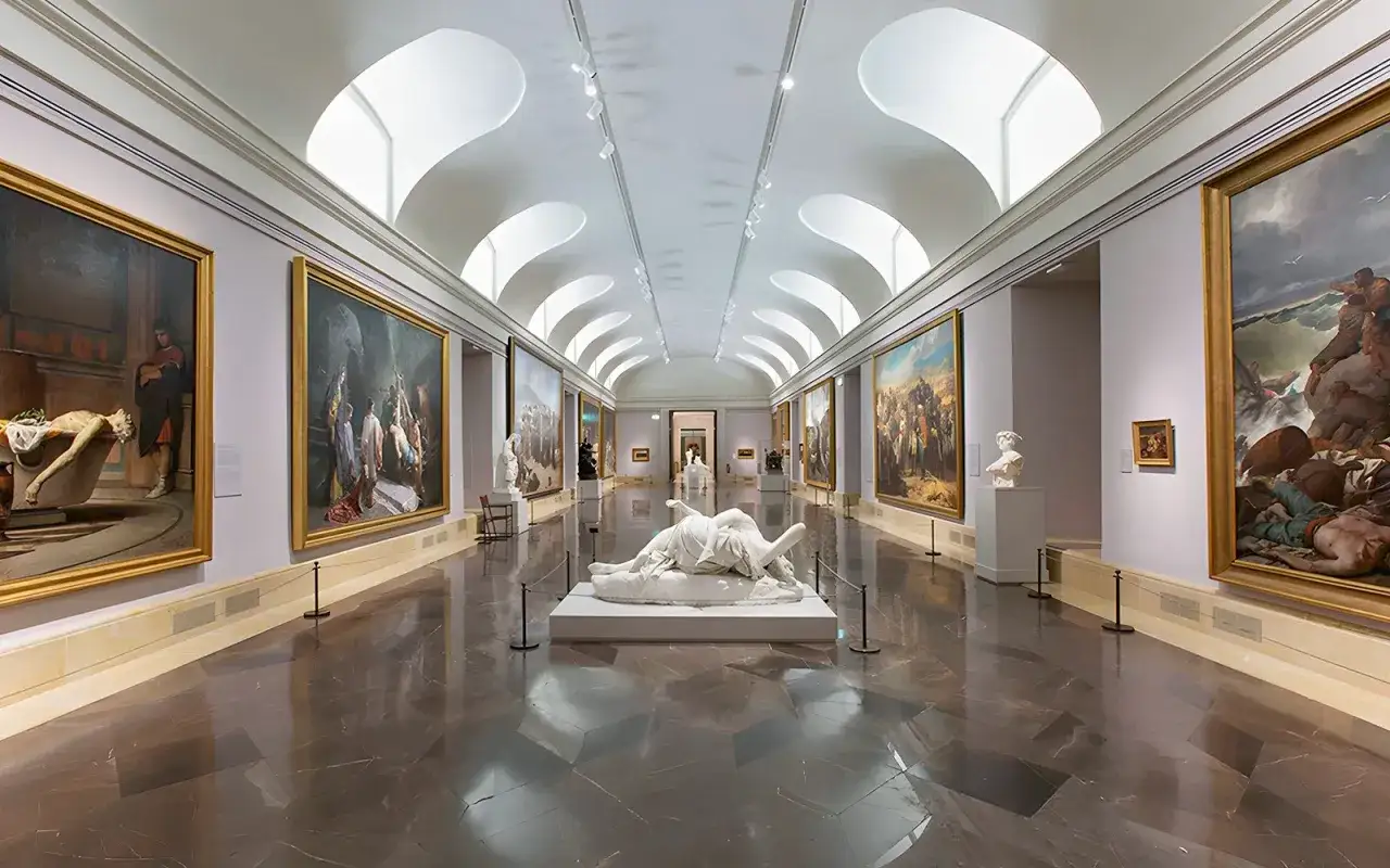 En l&aring;ng, ljus sal i ett konstmuseum i Madrid. Stora m&aring;lningar pryder v&auml;ggarna och en vit skulptur vilar i mitten.