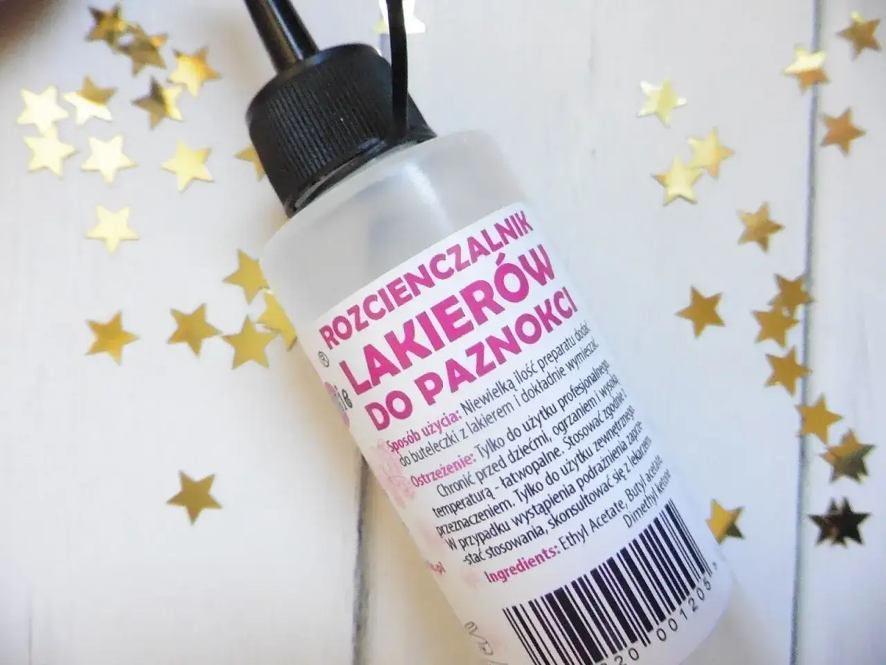 Butelka rozcieńczalnika do lakierów do paznokci, otoczona złotymi gwiazdkami. Idealne rozwiązanie, jak rozcieńczyć lakier do paznokci, by znów był jak nowy.