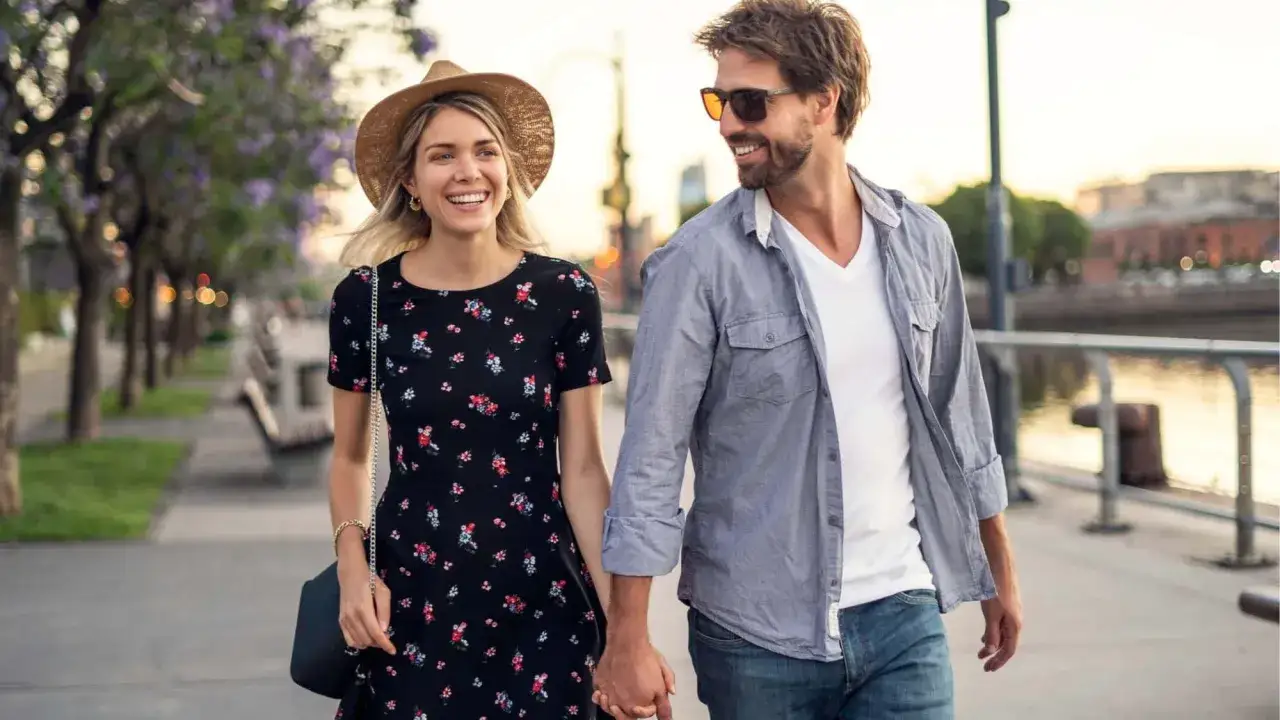 Gl&uuml;ckliches Paar spaziert Hand in Hand. Sein l&auml;ssiges Outfit: Jeans, wei&szlig;es T-Shirt, offenes Hemd. Perfekt f&uuml;r ein erstes Date Mann.