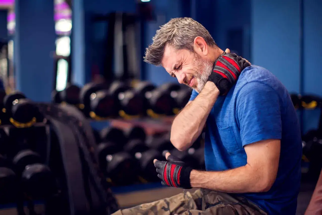 Uomo con guanti da palestra si tiene il collo, sofferente per il dolore al collo dopo palestra.