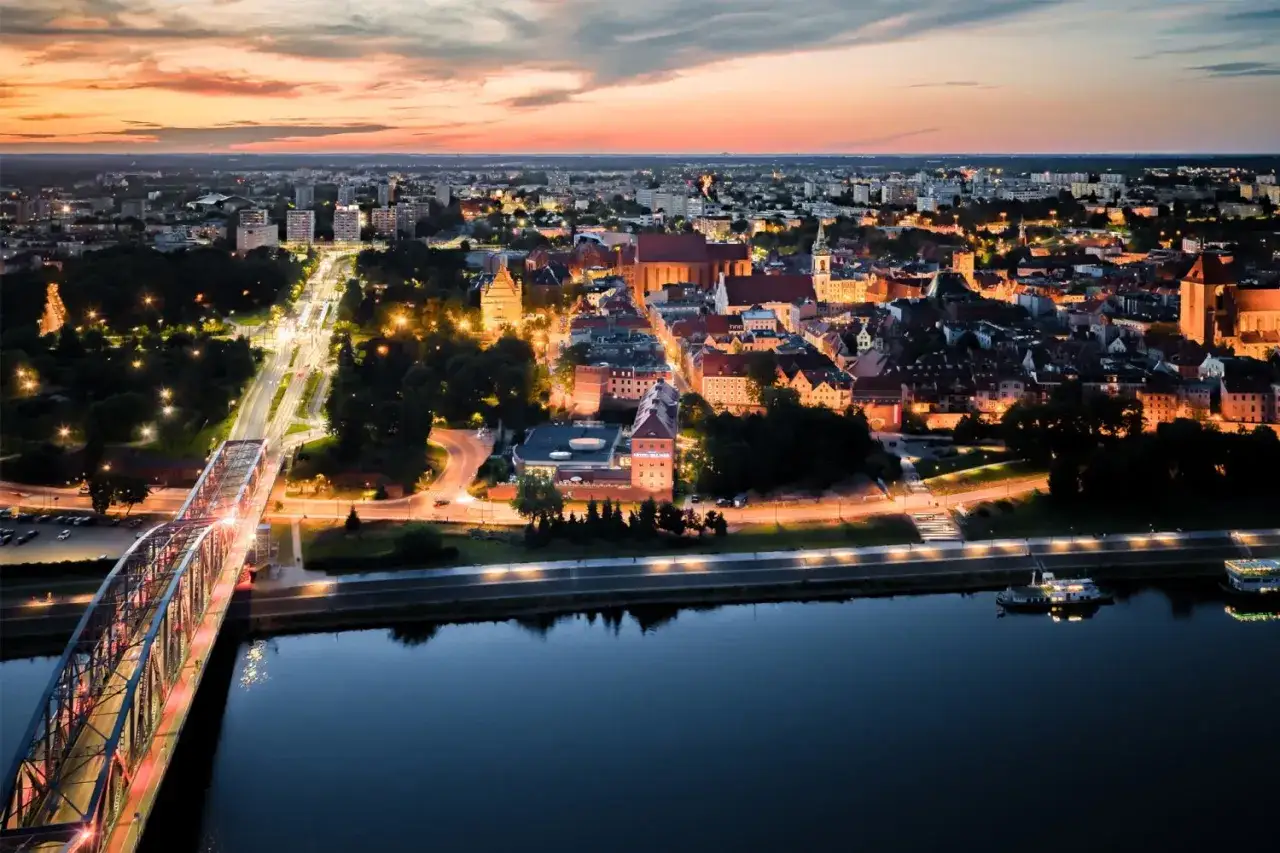 Piękne miasto nad Wisłą o zmierzchu. Most oświetlony, a w oddali widać zabytkowe budynki i nowoczesne bloki.