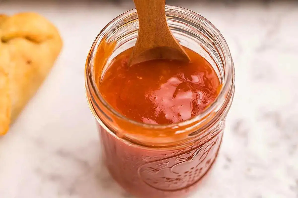 Cuill&egrave;re en bois dans un pot de sauce sucr&eacute; sal&eacute;, pr&ecirc;te &agrave; &ecirc;tre d&eacute;gust&eacute;e avec un morceau de pain dor&eacute;.