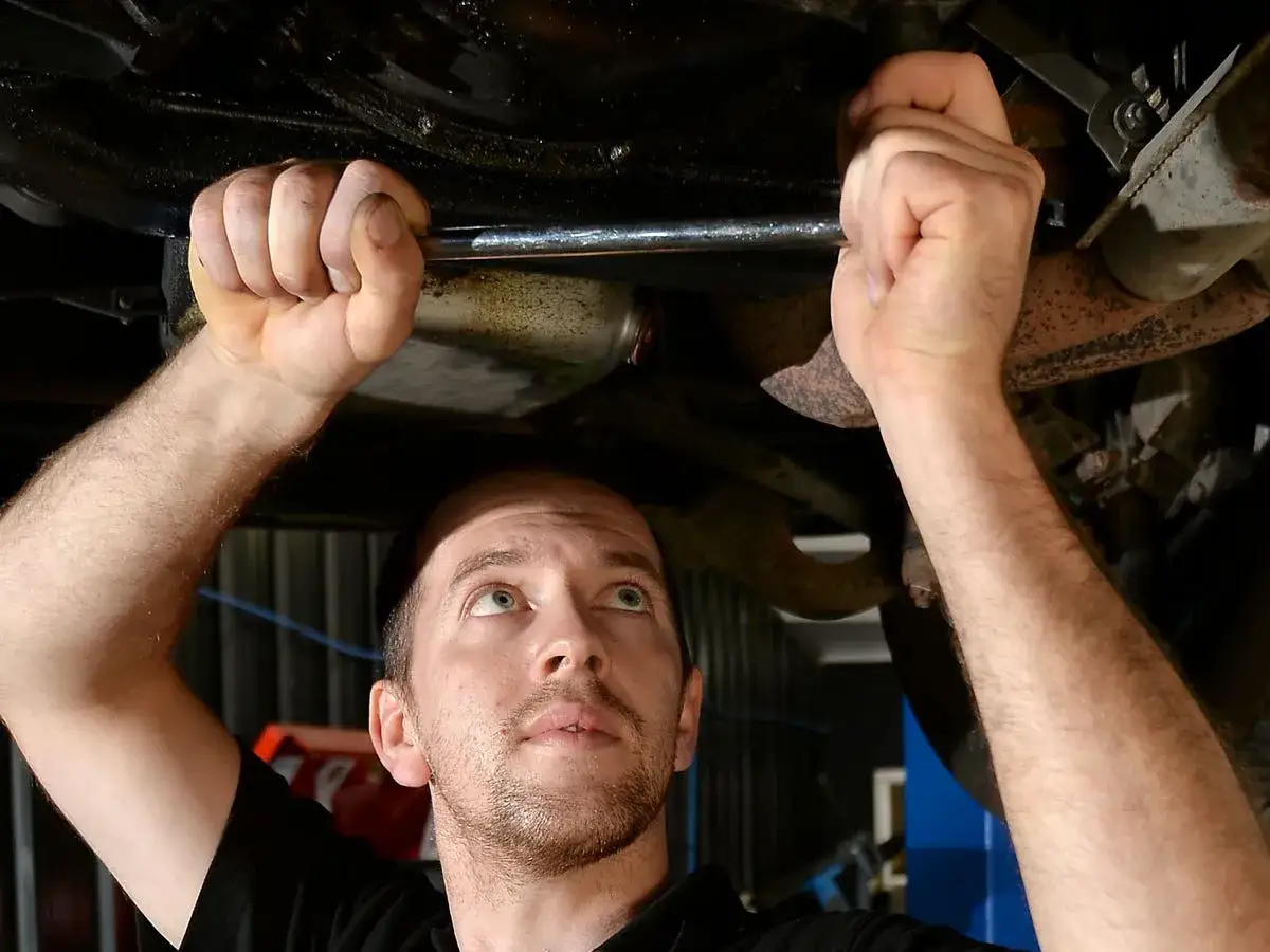 Hombre trabajando bajo un coche, usando una llave para aflojar un tornillo. Paso clave para saber como cambiar el aceite del coche.