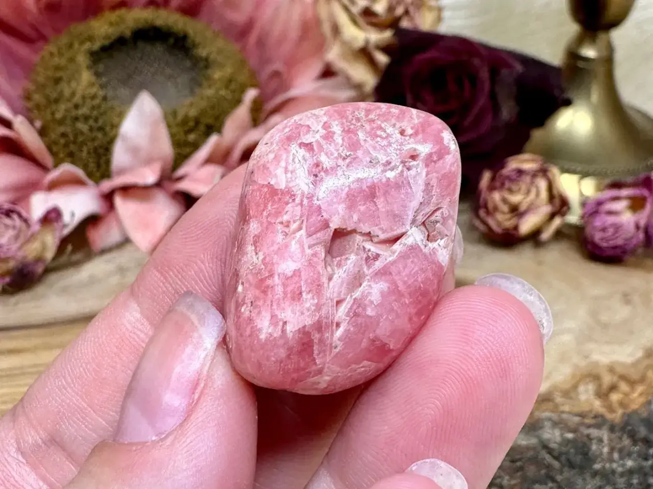 Ein pinker Rhodochrosit-Stein in einer Hand. Die Rhodochrosit Wirkung soll Liebe und Heilung fördern.
