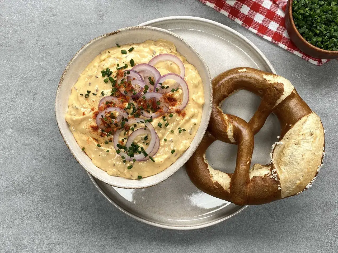 Obazda rezept: cremiger Käseaufstrich mit Zwiebelringen, Schnittlauch und Paprikapulver, dazu ein Brezn.