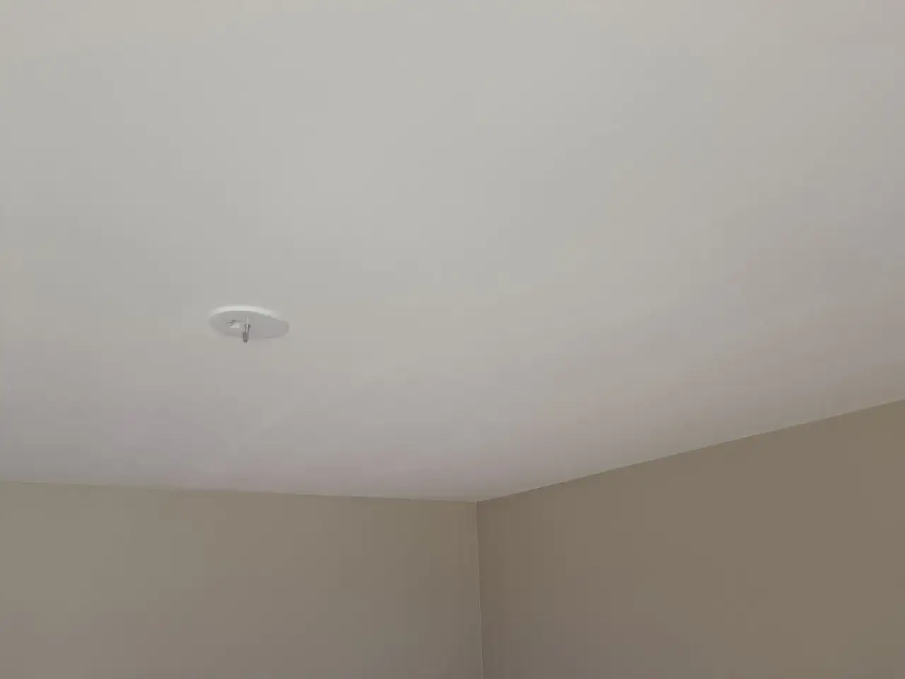 Ett vitt tak med en krok för en lampa. Väggarna är ljusbruna. Snart dags att måla taket för en fräschare känsla.