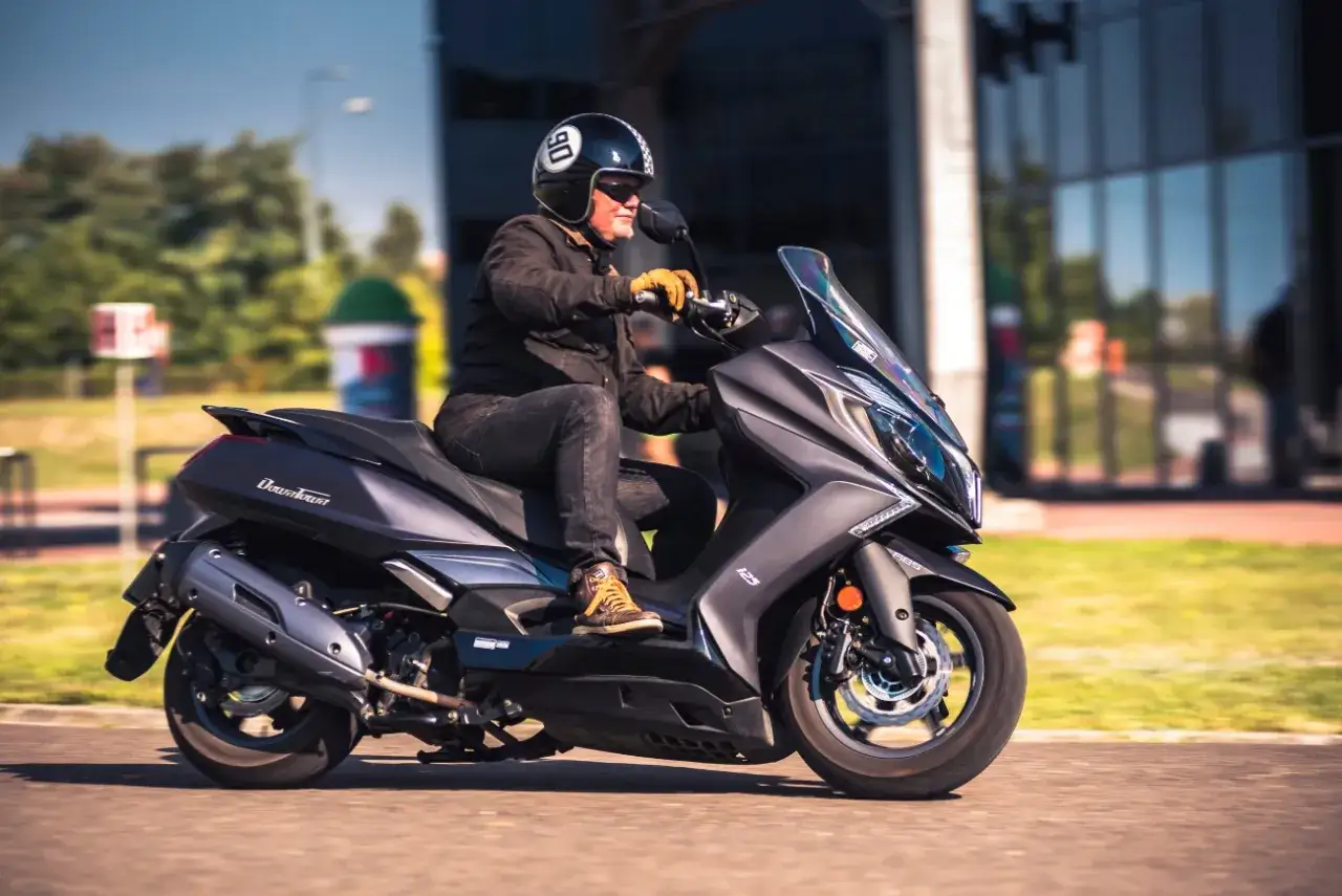 Mężczyzna w kasku jedzie na skuterze Kymco Downtown 125. Poznaj kymco downtown 125 dane techniczne.
