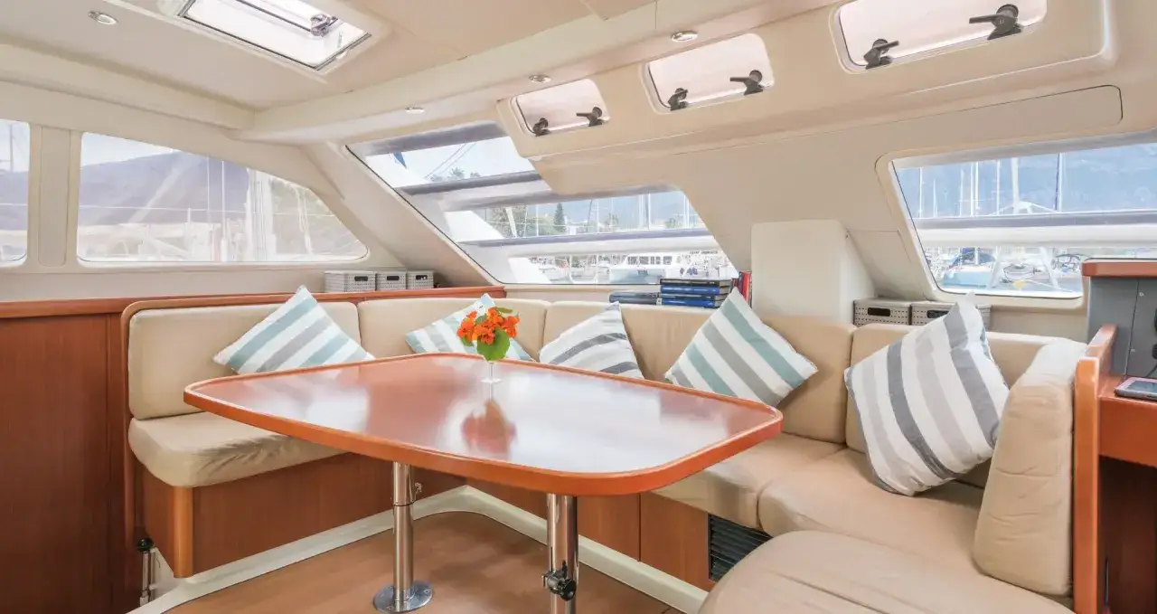 L'élégant **intérieur d'un voilier 8m** offre un espace de vie confortable avec des banquettes en cuir clair, des coussins rayés et une table en bois.