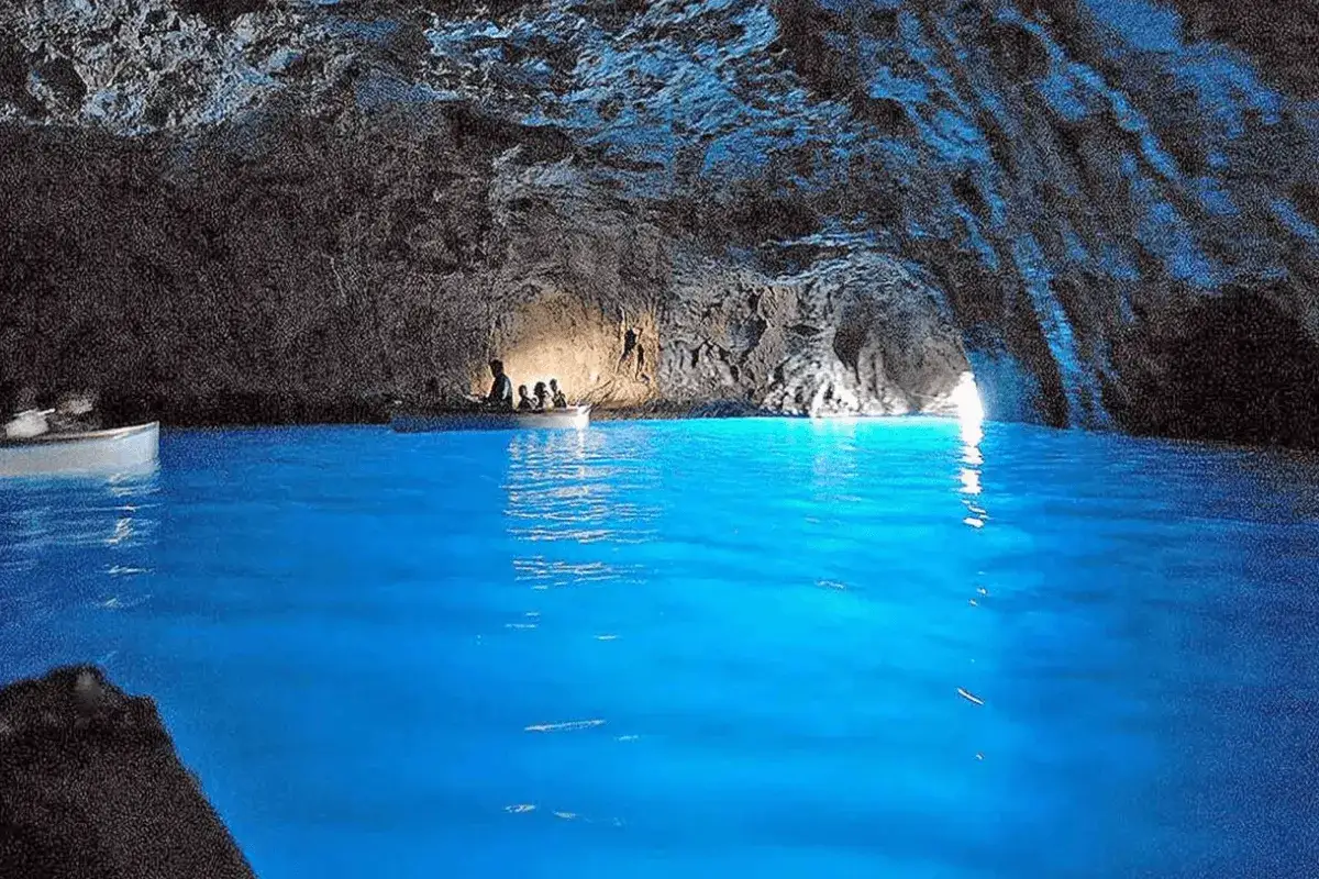 Gente in barca esplora la magica blue cave, con l'acqua che brilla di un blu intenso e le rocce scure che creano un'atmosfera surreale.