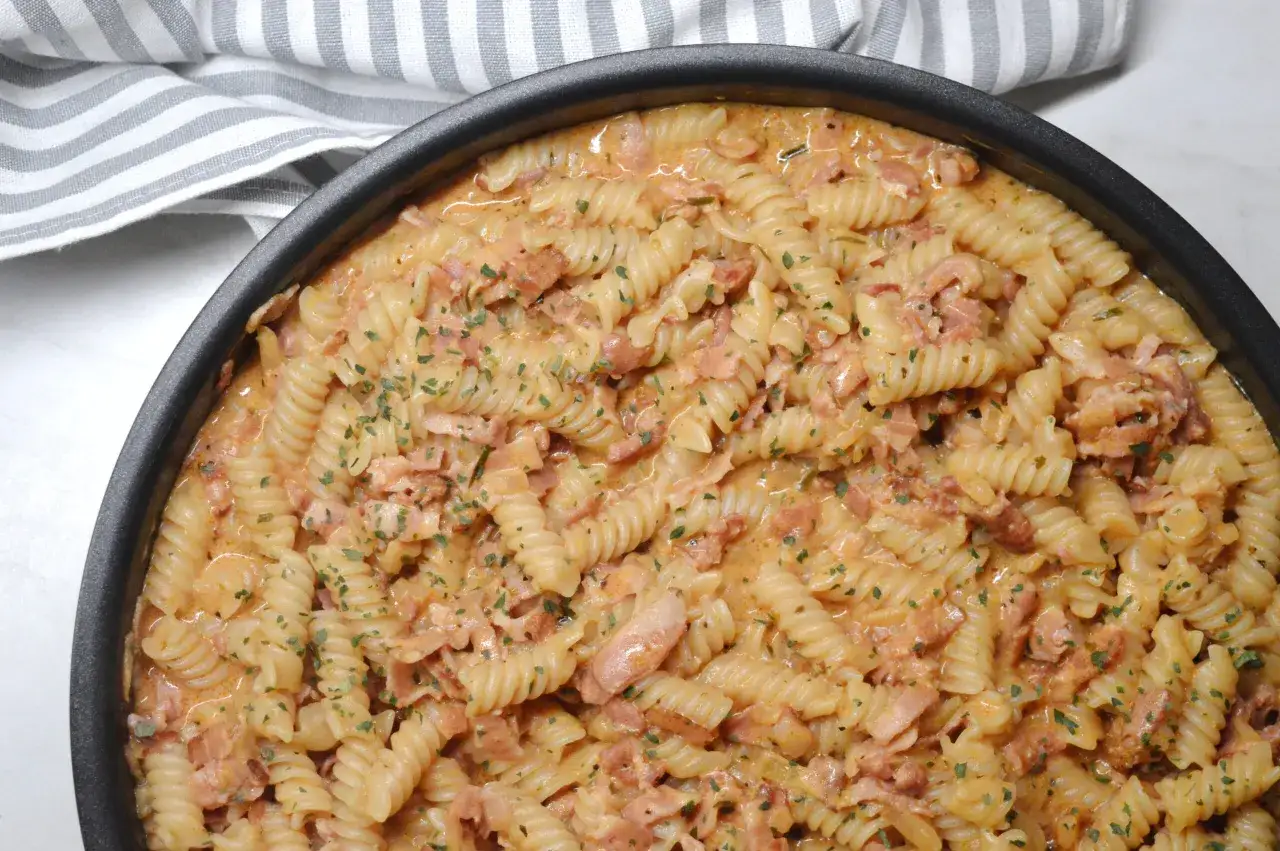 En kr&auml;mig pasta med bacon och persilja i en svart form, redo att serveras.
