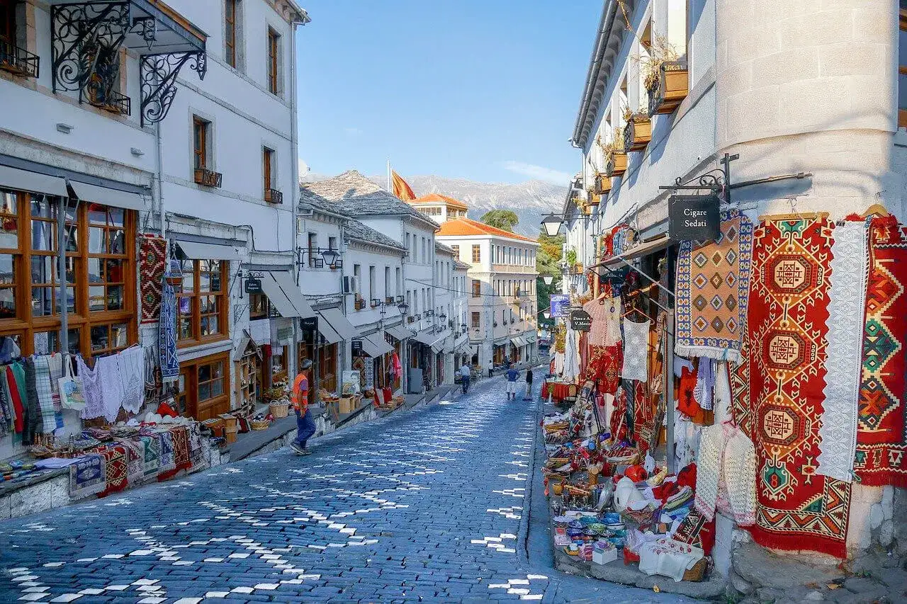 Słoneczna Albania we wrześniu. Brukowana uliczka pełna kolorowych dywanów i pamiątek, zachęca do spaceru.
