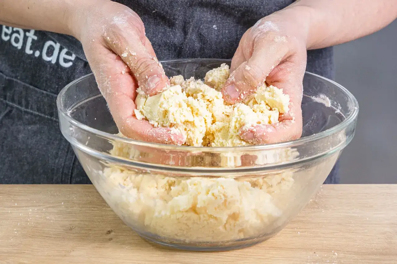 H&auml;nde verarbeiten Teig f&uuml;r ein einfaches Streusel Rezept in einer Glassch&uuml;ssel.