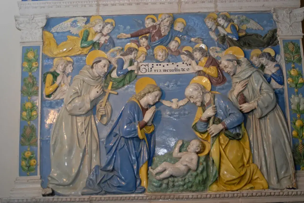 Della Robbia-Keramik: Geburt Christi mit Engeln und Heiligen. Maria kniet vor dem Jesuskind, Josef und Franziskus sind anwesend.