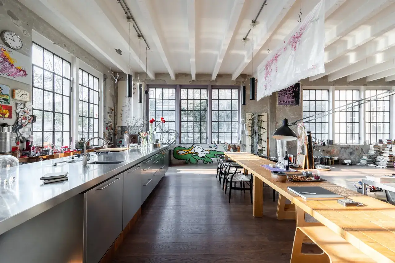 Ampio spazio aperto con cucina in acciaio, grande tavolo in legno e finestre industriali. Questo &egrave; cos'&egrave; un loft: un ambiente versatile e luminoso.