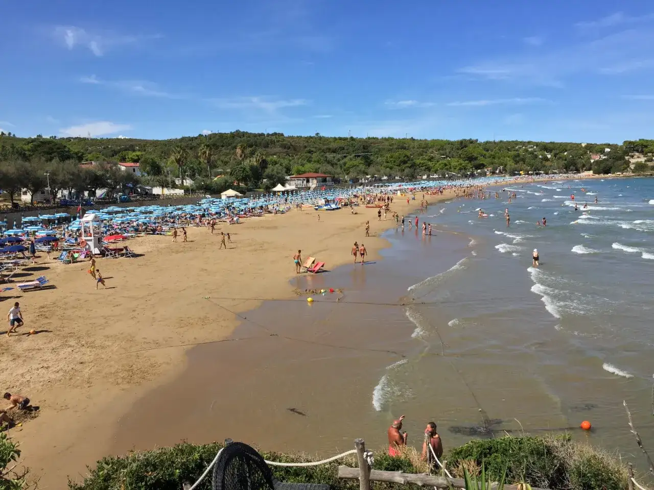 Una giornata di sole sulla spiaggia di Bescile, con ombrelloni, lettini e tante persone che si godono il mare e la sabbia.
