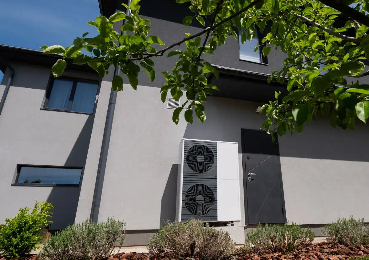 Unità esterna per riscaldamento elettrico, installata accanto a una casa moderna con giardino.