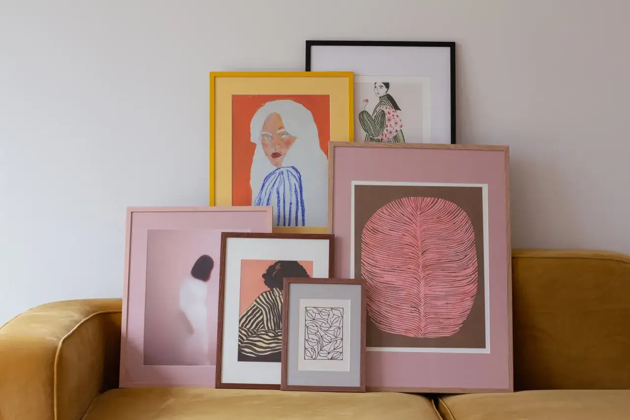 Kolekcja oprawionych grafik z paspartout, w tym portret kobiety z białymi włosami i ilustracja liścia, tworzy artystyczną kompozycję na kanapie.