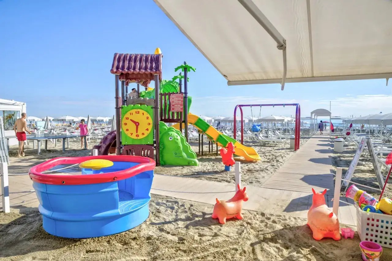 Area giochi su sabbia con scivolo, altalena e giochi d'acqua, un vero lido per bambini.