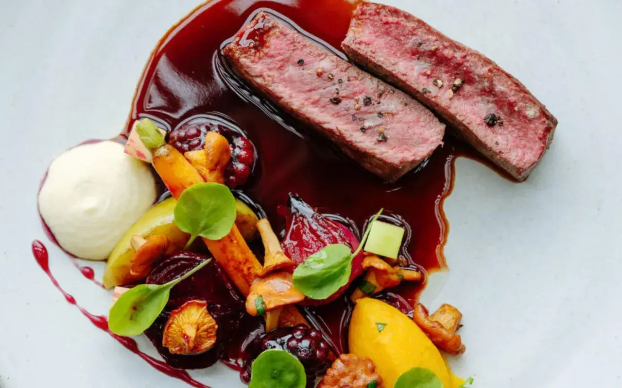 Tranches de b&oelig;uf juteuses napp&eacute;es d'une sauce viande rouge profonde, accompagn&eacute;es de l&eacute;gumes racines color&eacute;s et d'une pur&eacute;e onctueuse.